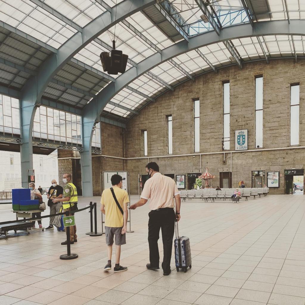 Un adolescente y un hombre adulto que se alejan juntos en una estación de tren hacia la zona de embarque. La foto está tomada de espaldas.