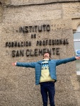 Un chico adolescente mira al cielo con los brazos extendidos junto a un edificio que señala en su fachada "Instituto de Formación profesional San Clemente"