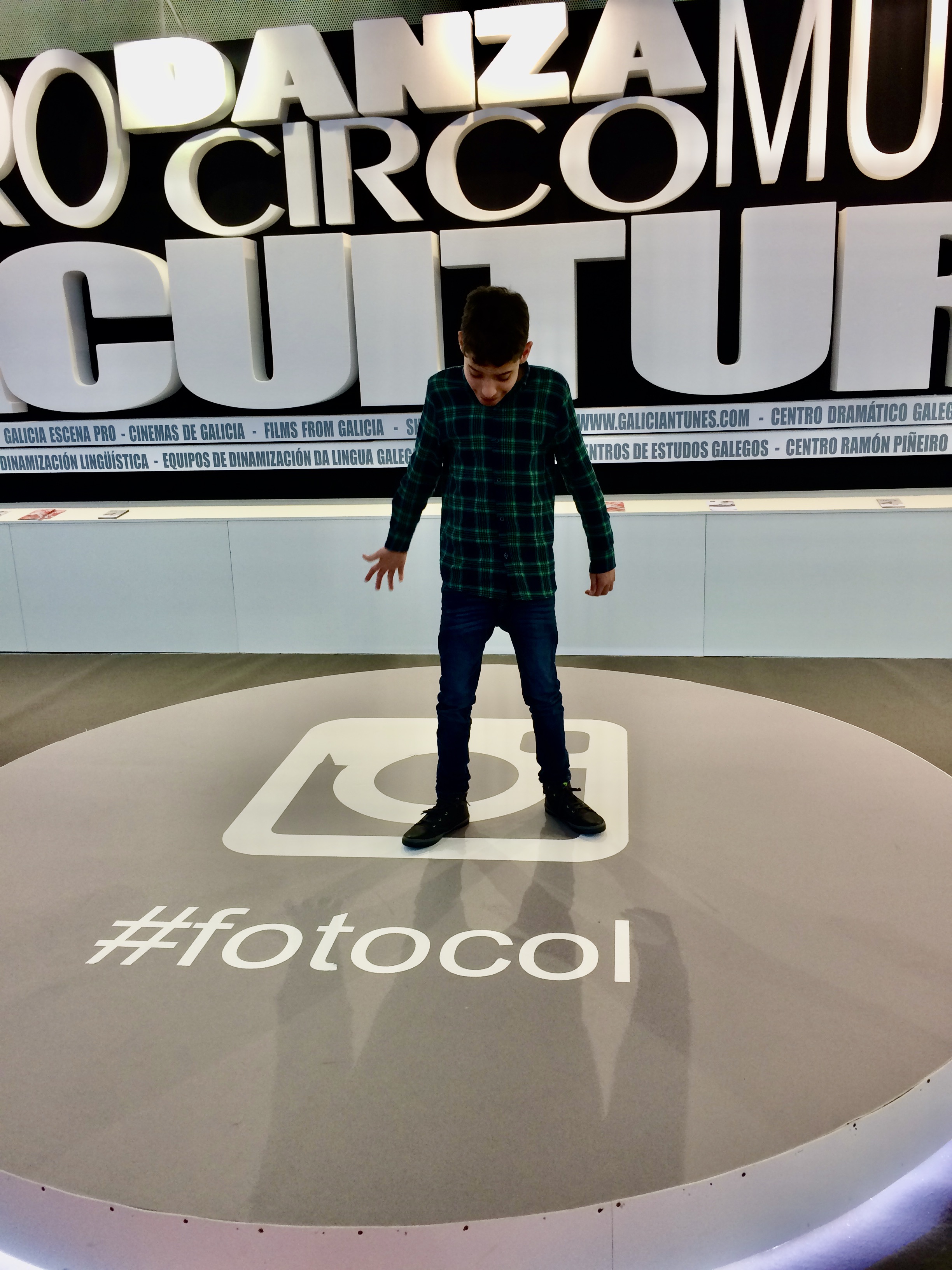 Foto donde aparece un niño de unos ocho años posando en un photocall instalado en el transcurso de una edición del Culturgal (feria de la industria cultural gallega). En el suelo, junto al logo de instagram aparece escrito “#fotocol”. En la pared del fondo pueden verse diferentes palabras a gran tamaño y en tres dimensiones: danza, circo, cultura, música.