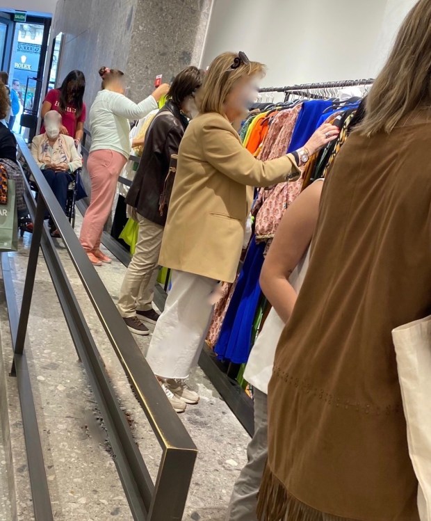 interior de una tienda de ropa de una gran multinacional. Se muestra una rampa donde una usuaria en silla de ruedas está a la espera de que la rampa se despeje para poder pasar. En la pared pegada a la rampa se ha colocado una barra con vestidos y los clientes utilizan la rampa para valorar las prendas. La rampa pasa de ser un recurso de accesibilidad a convertirse en un espacio más de consumo. 