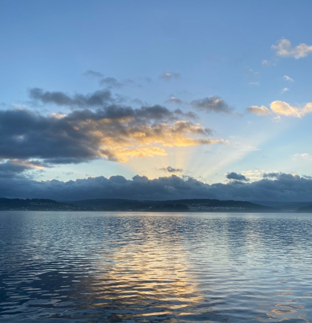 Foto de una amanecer sobre el mar. Se aprecia asomando el sol entre la bruma baja, la parte superior del cielo es de un azul intenso