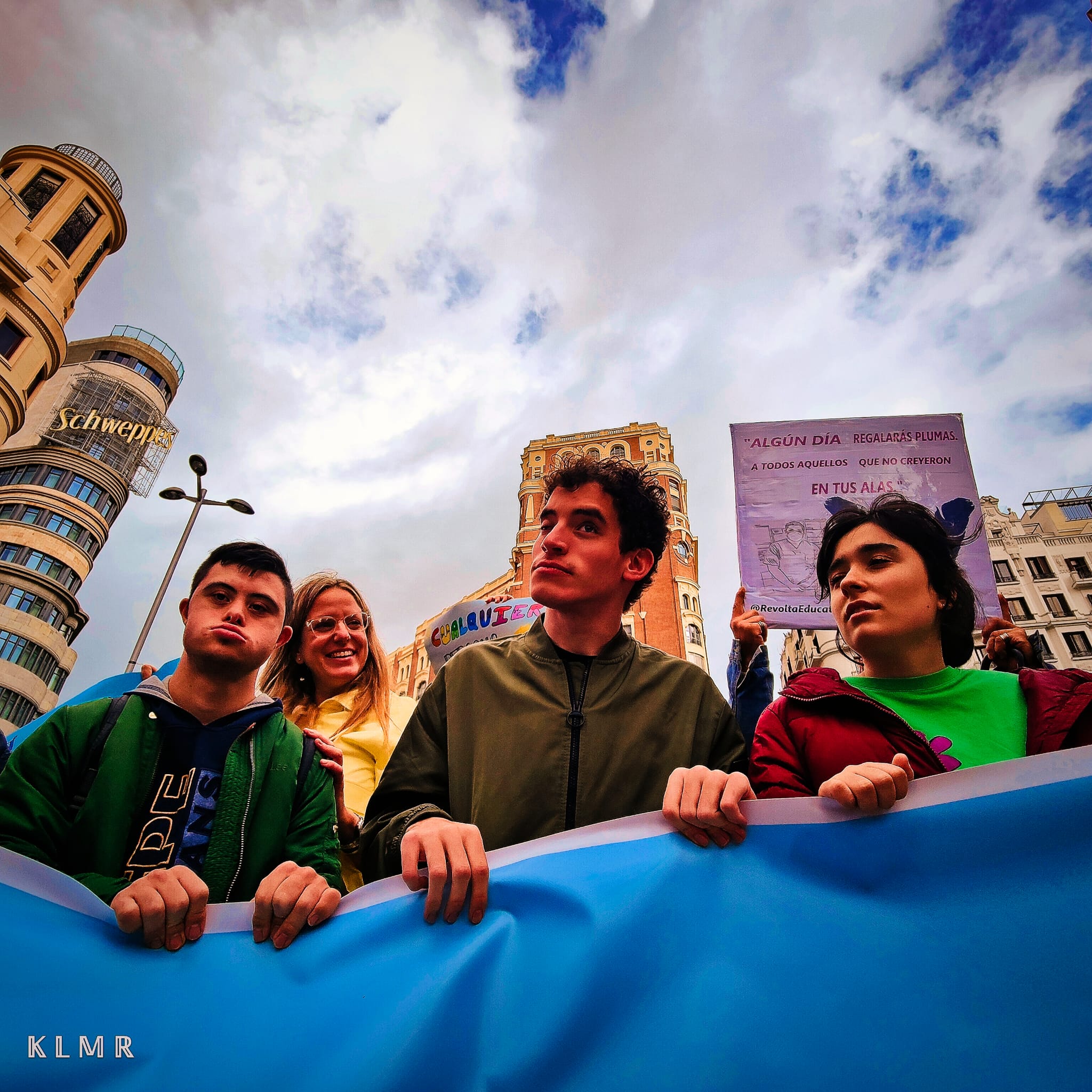 Imagen donde se ve a tres adolescentes (dos chicos y una chica) sujetando una pancarta azul en la cabeza de una concentración.