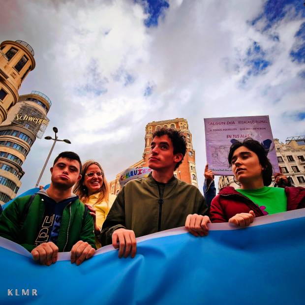Imagen donde se ve a tres adolescentes (dos chicos y una chica) sujetando una pancarta azul en la cabeza de una concentración.