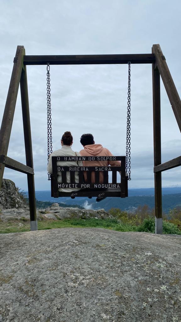 Imagen donde se ve de espaldas a un chico y una chica sentados en un columpio.