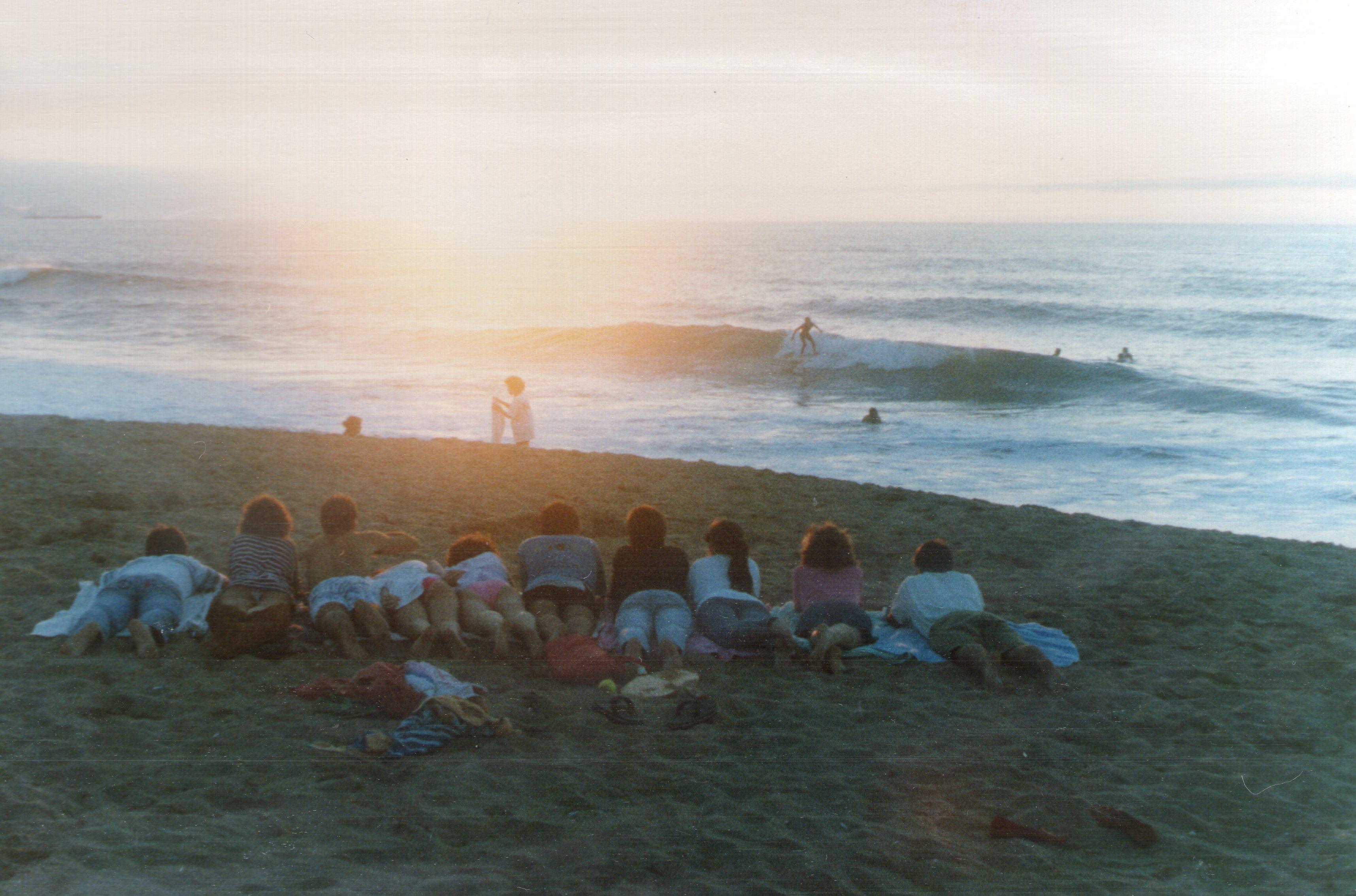 Grupo de adolescentes tumbados de espaldas viendo el atardecer en la play