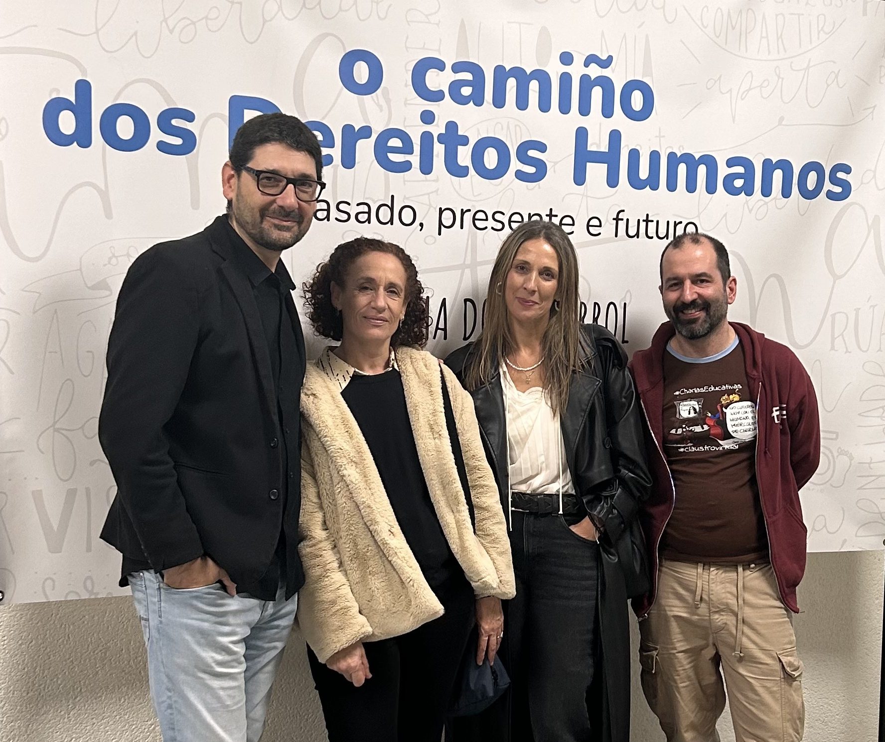 Fotografía donde aparezco con otros tres asistentes a la jornada. Detrás se ve el cartel de las jornadas donde puede leerse “O camiño dos Dereitos Humanos: presente, pasado e futuro”.