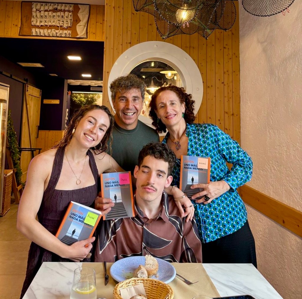 Antón sentado a la mesa de un restaurante. Le rodean, de pie, su hermana, su padre y su madre. Cada uno de ellos sostiene y muestra a cámara un ejemplar del libro de Antón.